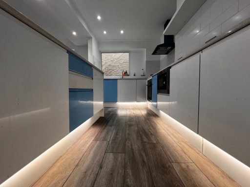 Modern kitchen with sleek cabinetry, wooden flooring, and ambient lighting.